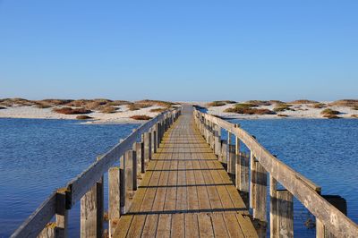 Pier over sea against clear blue sky