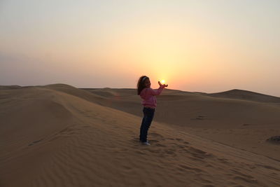 Girl catching sun with her hands on dubai's desert