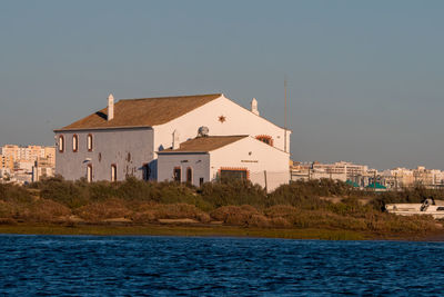 Houses by sea against buildings in city against clear sky