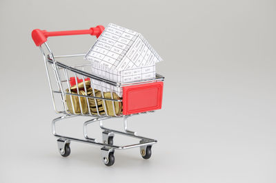 Close-up of coins and model house in shopping cart over gray background