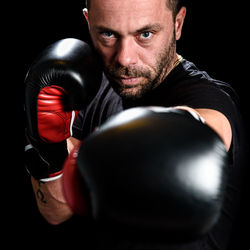 Portrait of mid adult man wearing boxing gloves against black background