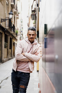 Stylish mid adult man with arms crossed standing by wall in city