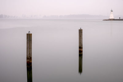 Wooden post and lighthouse on sea against sky