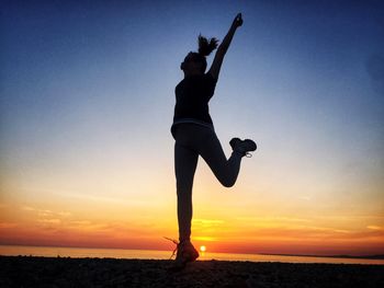 Silhouette woman jumping at beach against sky during sunset