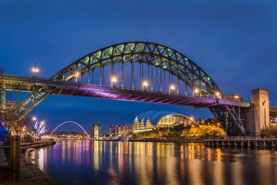 Illuminated bridge over river against sky at night