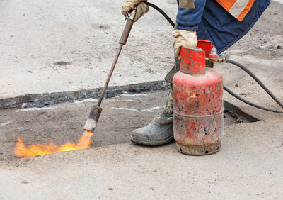 Patching a road by heating a damaged asphalt surface with a gas burner.