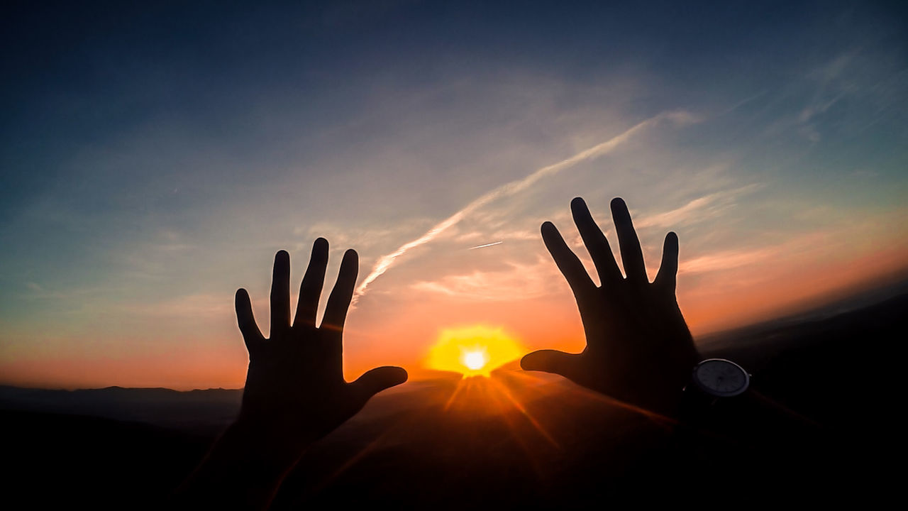 SILHOUETTE OF PERSON HAND AGAINST SUNSET SKY