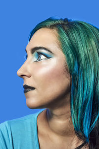 Close-up portrait of a young woman against blue background