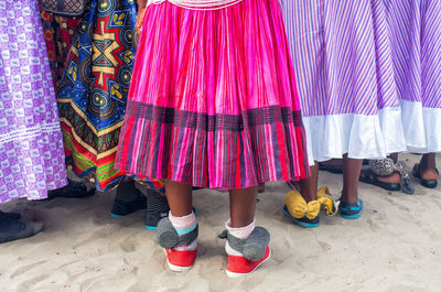 Low section of women wearing colorful skirts standing on sand