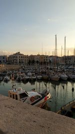 Sailboats moored in harbor at sunset