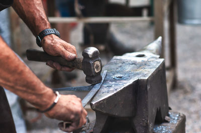 Cropped hands of blacksmith hammering metal on anvil
