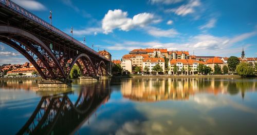 Reflection of bridge and buildings in river against sky