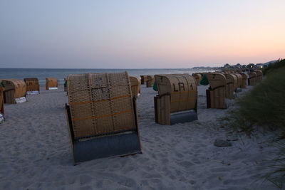 Hooded chairs on beach against sky during sunset