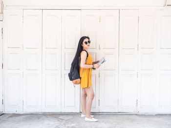 Full length portrait of woman standing against wall