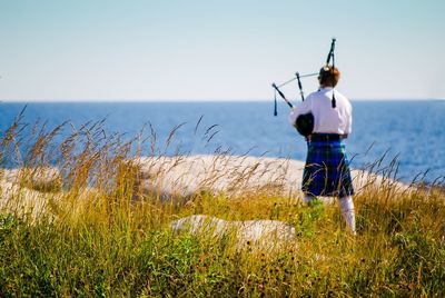 Rear view of person holding bagpipe by sea against sky