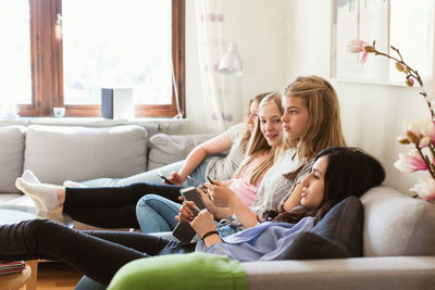 Side view of teenage girls watching tv while relaxing on sofa at home