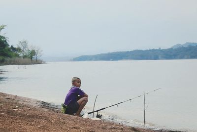 Boy fishing in lake against sky