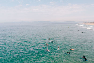 Surfers swimming on sea against sky