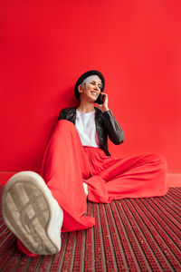 Young woman looking away while sitting on mirror against red wall