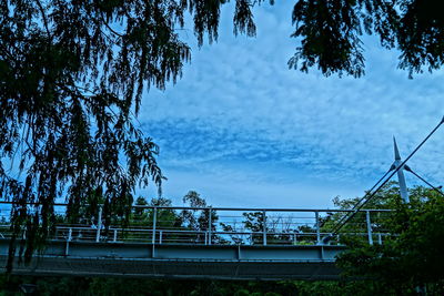 Trees by bridge in city against sky