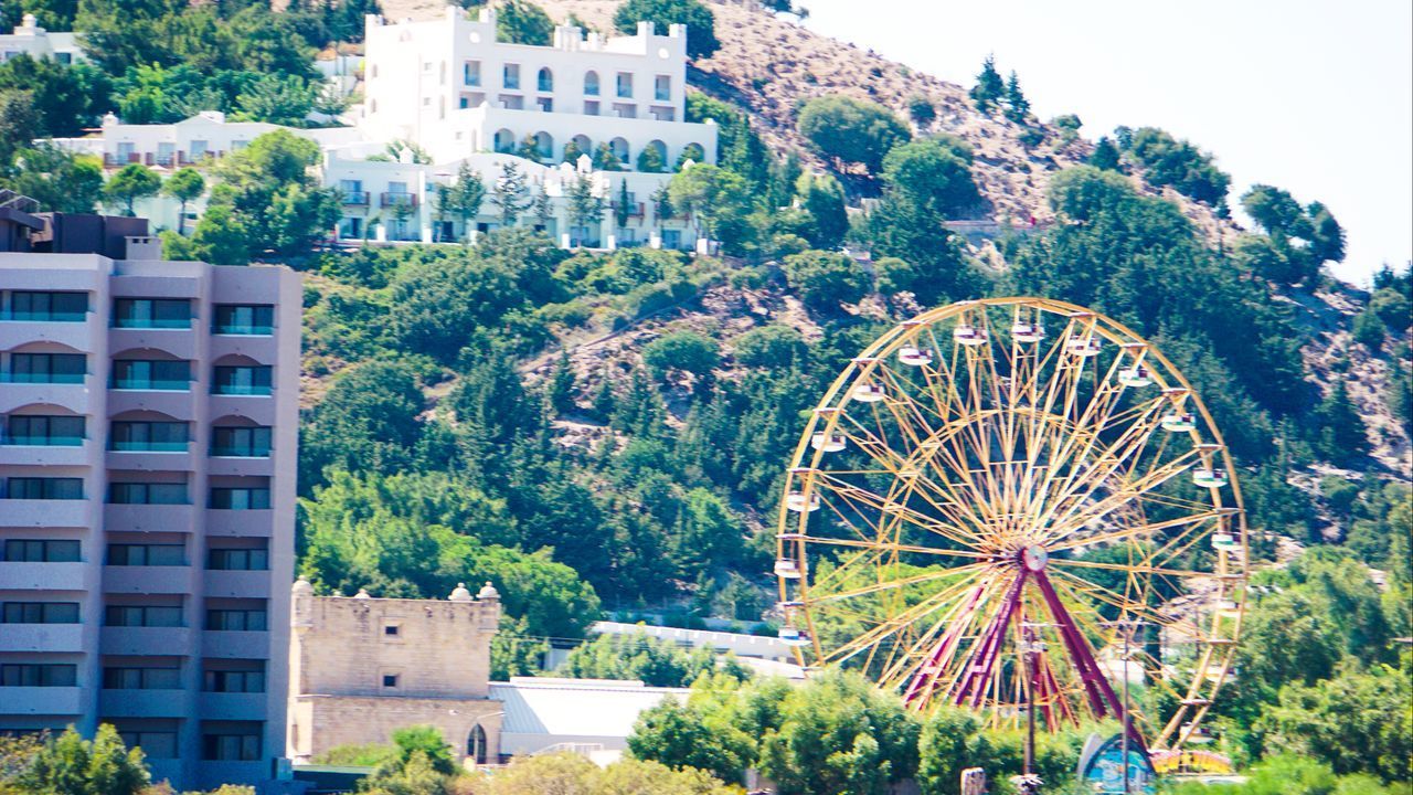 FERRIS WHEEL BY BUILDINGS AGAINST SKY