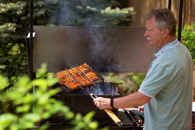 Senior man grilling in the backyard of his country house in sunny summer day. backyard barbecue.