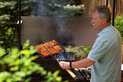 Side view of man preparing food on barbecue grill