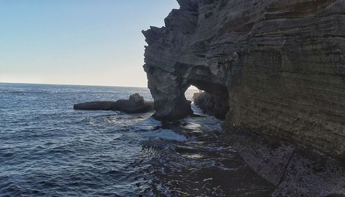 Rock formation in sea against clear sky