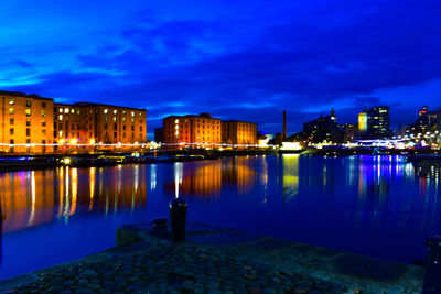 Illuminated buildings by river against sky at night