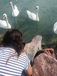 Woman with mobile phone sitting on rock formation by swans at lake