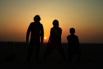 Silhouette people standing on beach during sunset