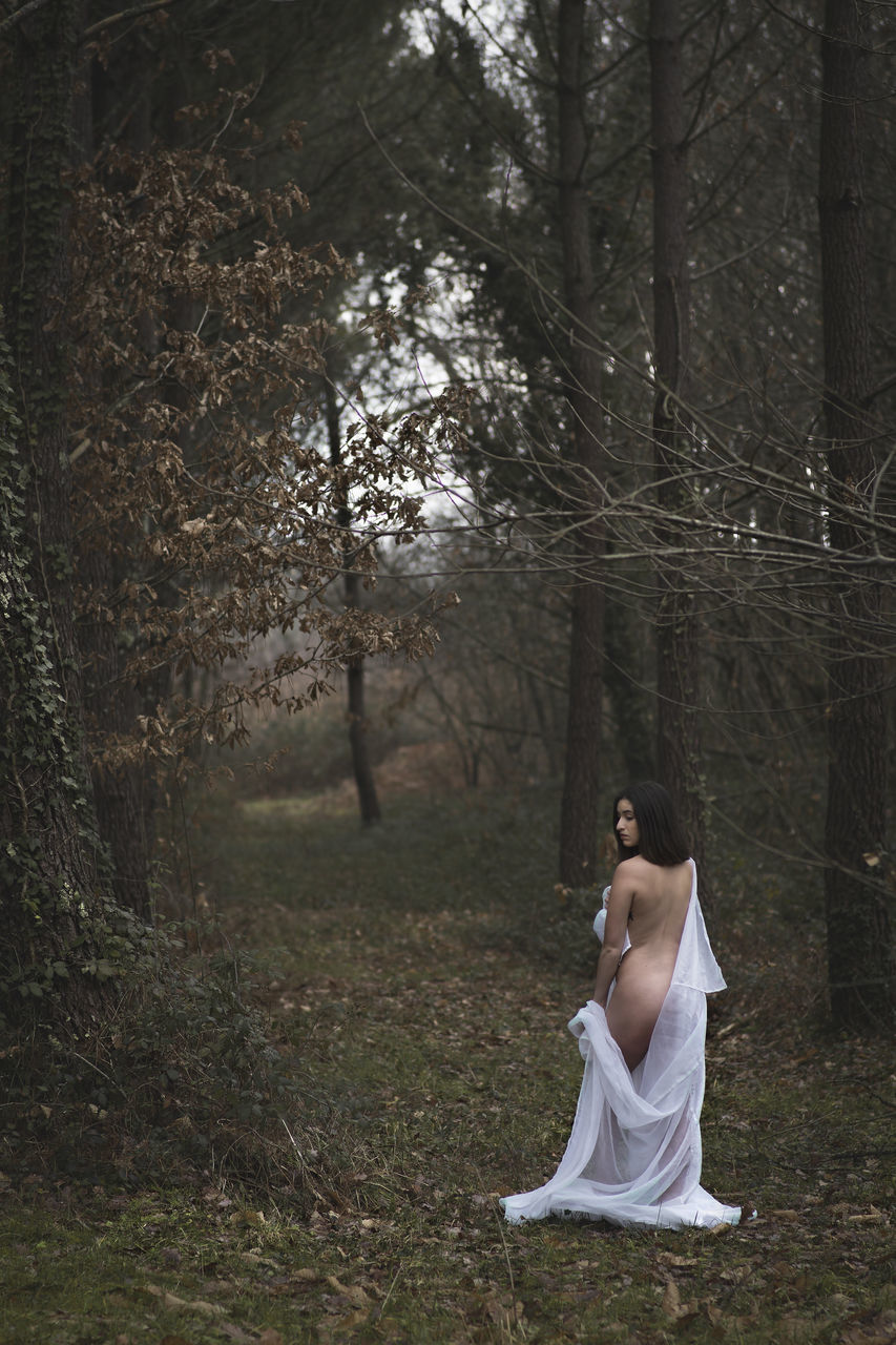 forest, tree, land, one person, plant, full length, women, adult, sitting, tranquility, nature, clothing, dress, lifestyles, young adult, tree trunk, leisure activity, real people, woodland, day, fashion, outdoors, hairstyle, contemplation