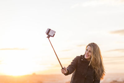 Young woman using phone while standing against sky