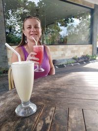 Portrait of a smiling young woman with drink on table