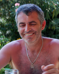 Close-up of shirtless smiling man against plants
