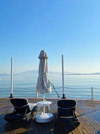 Chairs and table by sea against clear sky