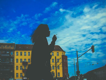 Low angle view of silhouette woman standing by buildings against sky