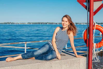 Portrait of smiling woman sitting by sea against sky