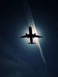 Low angle view of silhouette airplane flying against blue sky