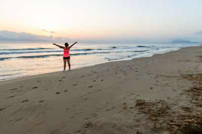 Rear view of woman with arms outstretched at beach against sky