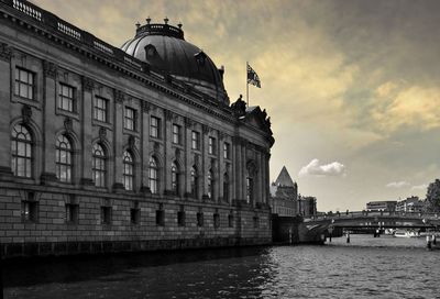 View of building by river against cloudy sky