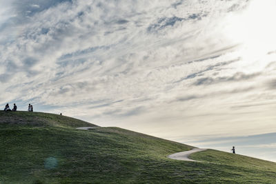 People on hill against cloudy sky