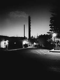 Illuminated street by buildings against sky at night