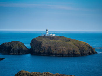 Lighthouse on island amidst sea against blue sky