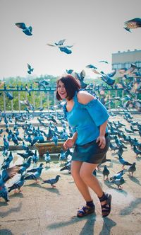 Full length of mid adult woman dancing by birds on footpath against sky