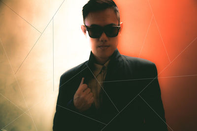 Portrait of young man wearing sunglasses standing against wall