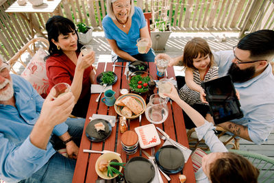 High angle view of family toasting drink glasses while having food at table in patio