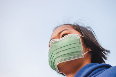 Close-up of girl wearing pollution mask against sky