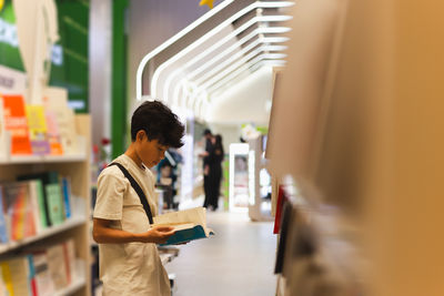 Side view of young boy reading book in a book store.