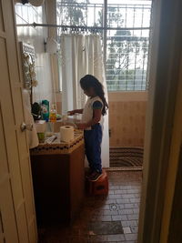 Side view of woman standing by window at home